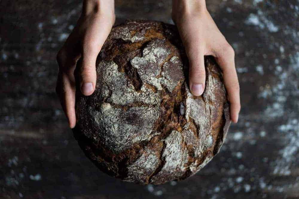 Knuspriges, dunkelbraunes Brot umfasst von zwei Händen in Nahaufnahme