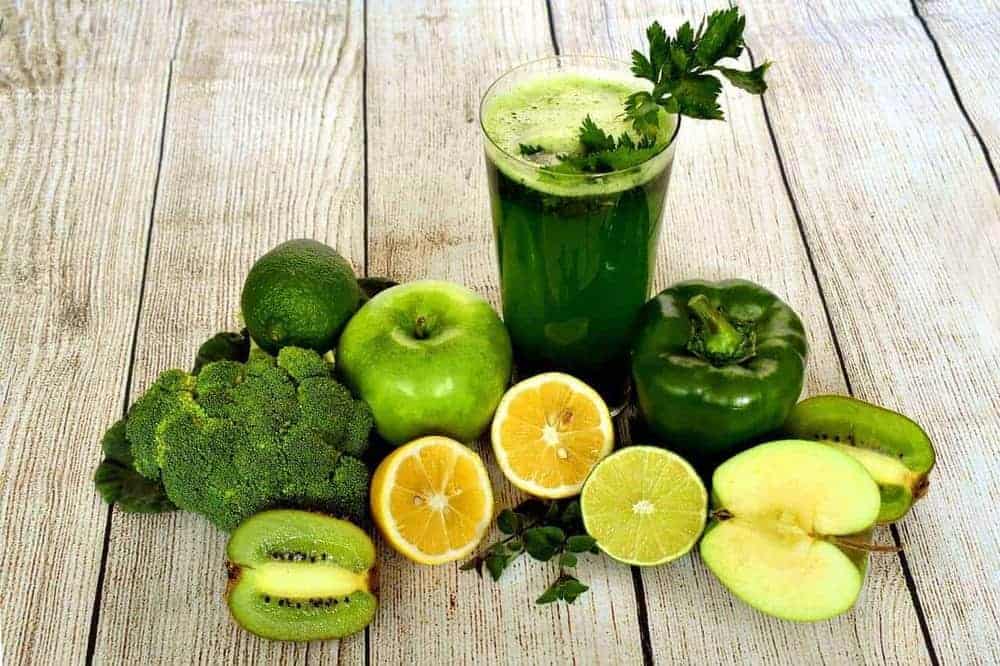 Grünes Obst und Gemüse mit einem Glas voll grünem Saft im Zentrum auf einem Holztisch