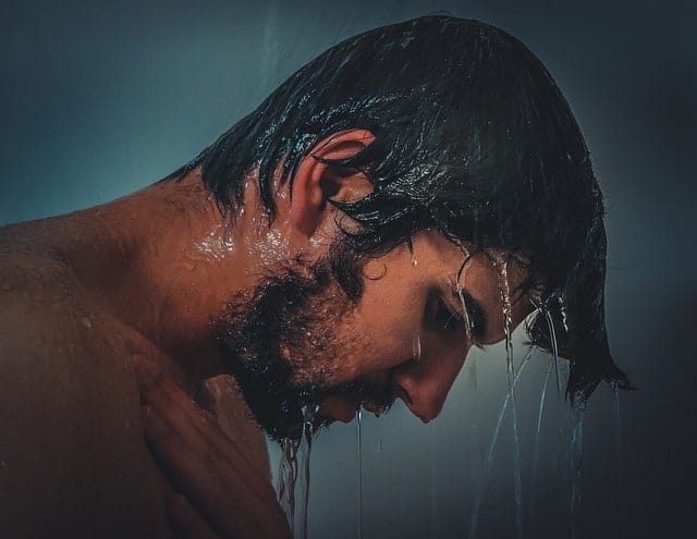 Junger Mann unter Dusche mit blauem Hintergrund