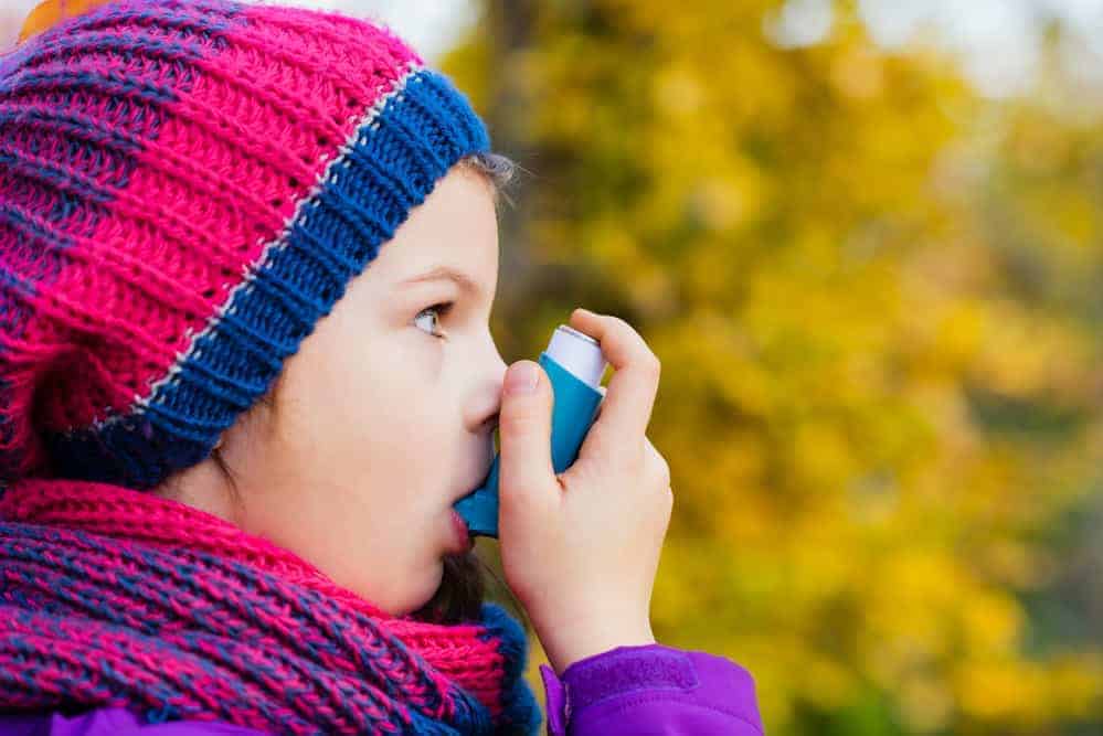 Mädchen mit Inhalator im Herbst mit Mütze um Asthma zu behandeln