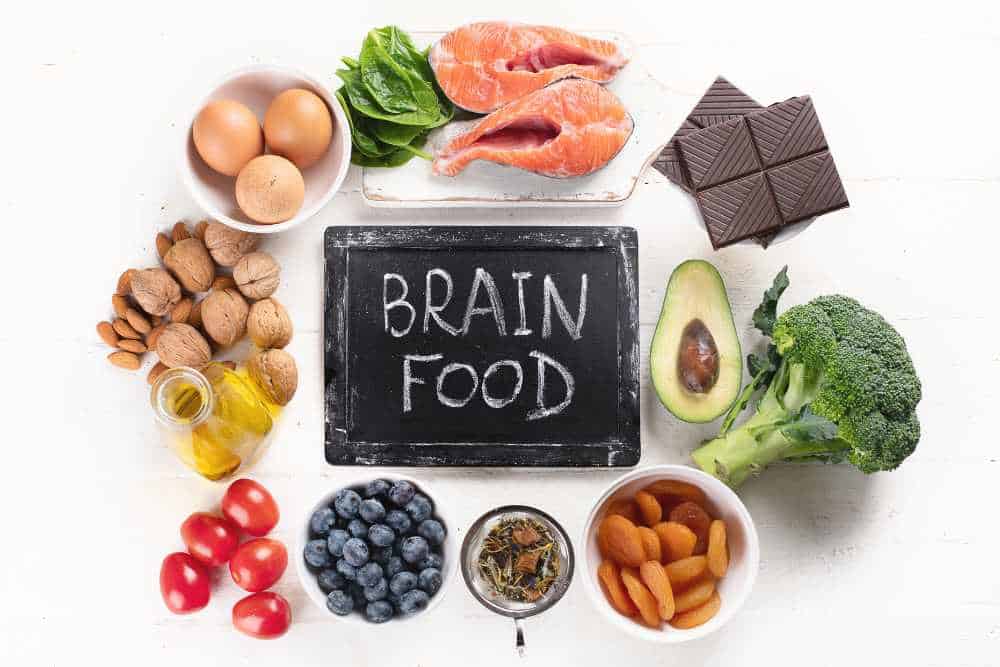 Brainfood als Wort auf einer Tafel, darum herum sind Lebensmittel angeordnet wie Eier und Blaubeeren