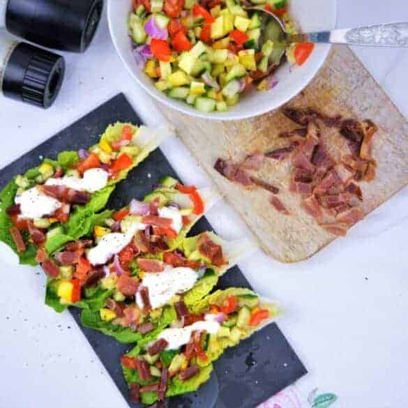 Salat Tacos auf Schieferbrett neben Kochutensilien auf weißer Platte