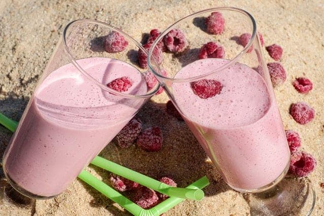 Zwei Gläser mit rosafarbenem Himbeer-Proteinshake auf Strand