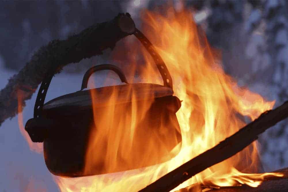 Topf in offenem Feuer mit Winterwald im Hintergrund