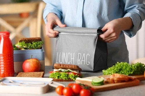 Gesunde Sandwiches neben Saftflasche und Zutaten mit Lunch Bag im Hintergrund