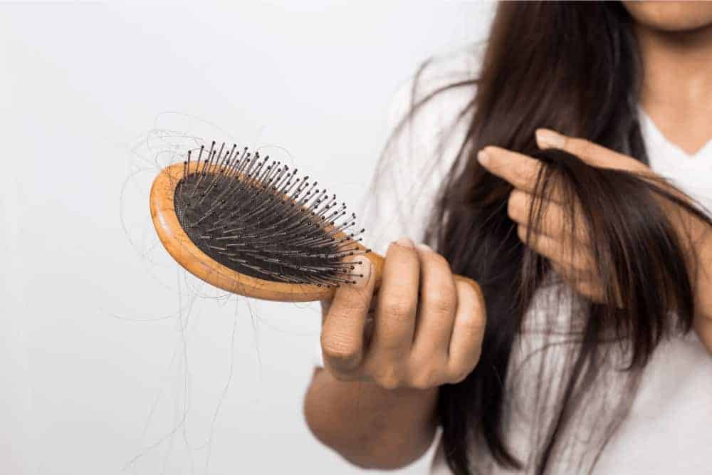Frau mit Haarausfall hält Bürste vor sich