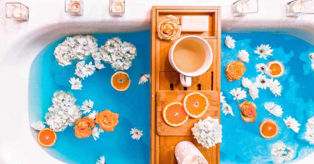Erkältungsbad als Hausmittel gegen Fieber. Mit Blüten und Orangenscheiben dekorierte Badewanne mit Kerzen