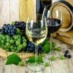 Weißwein- und Rotweinglas mit Trauben auf Holztisch