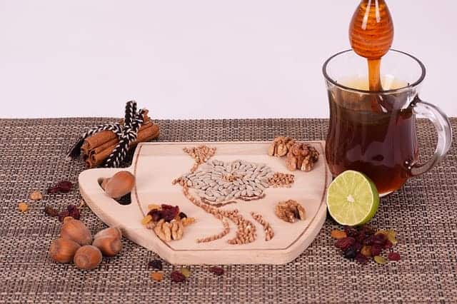 Nüsse und Zimtstangen auf Holzbrett, daneben eine Teetasse, die mit Honig gesüßt wird