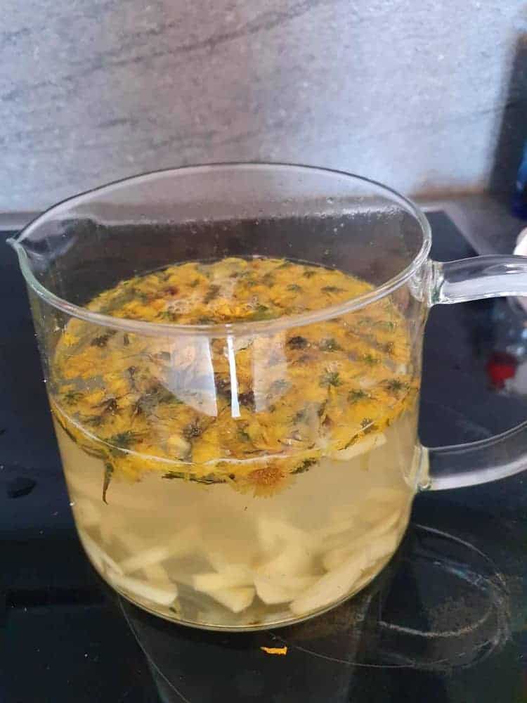 Offene Teekanne aus Glas mit Blüten auf Herdplatte