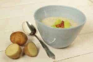 Kartoffeln neben Löffel neben weisser Suppenschale auf hellem Tisch