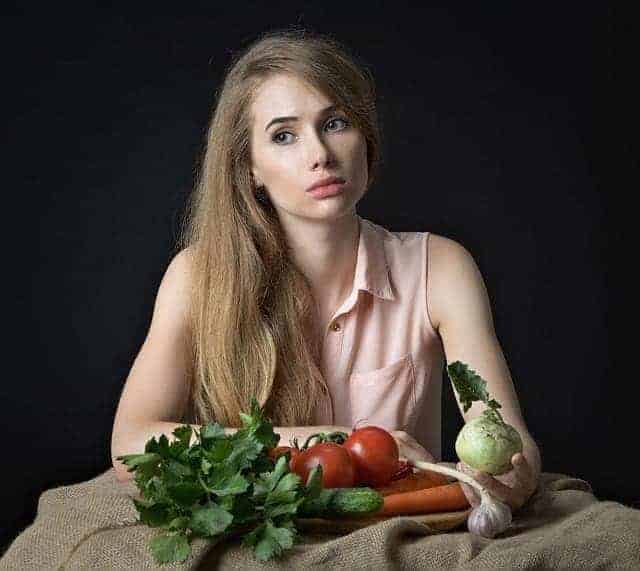 Junge Frau sitzt nachdenklich vor frischem Gemüse, das auf einem Leintuch ausgebreitet ist