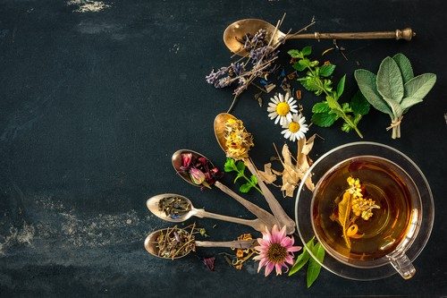 Verschiedene Blüten, Gewürze und Kräuter und Tasse Kamillentee auf dunklem Holztisch