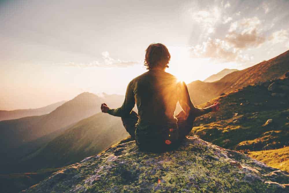 Mann beim meditieren lernen auf einer Bergspitze im Sonnenuntergang
