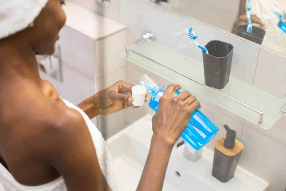 Junge Frau gießt Mundspülung in Becher vor Badezimmerspiegel