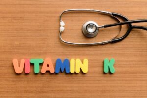Ein Stethoskop liegt auf einem Holztisch. Buchstaben formen das Wort Vitamin K