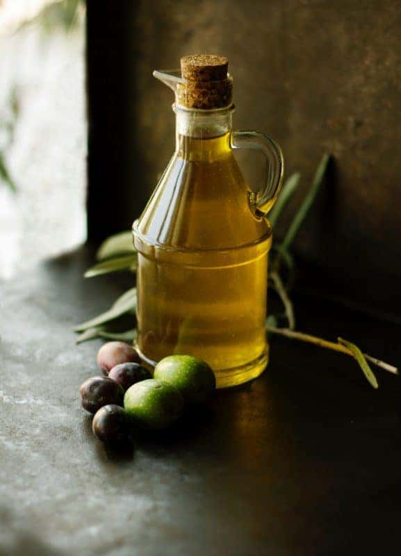 Flasche Olivenöl mit frischen Oliven auf schwarzer Platte