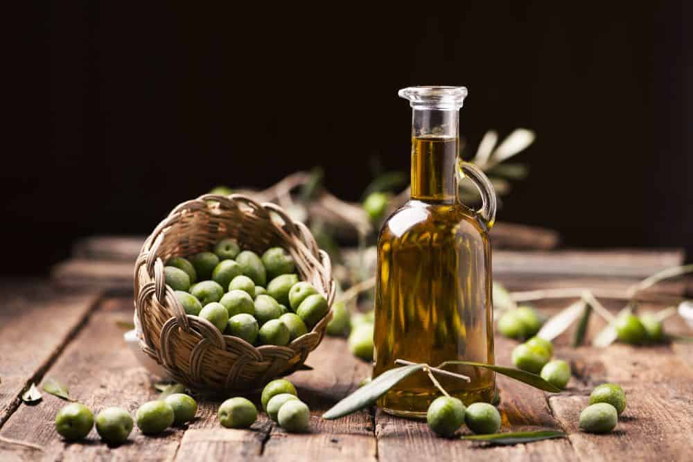 Oliven in einem Holzkorb und eine Flasche Olivenöl auf einem Holztisch