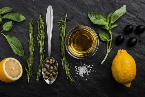 Olivenöl, mediterrane Kräuter, Zitrone und Oliven auf einer schwarzen Schieferplatte