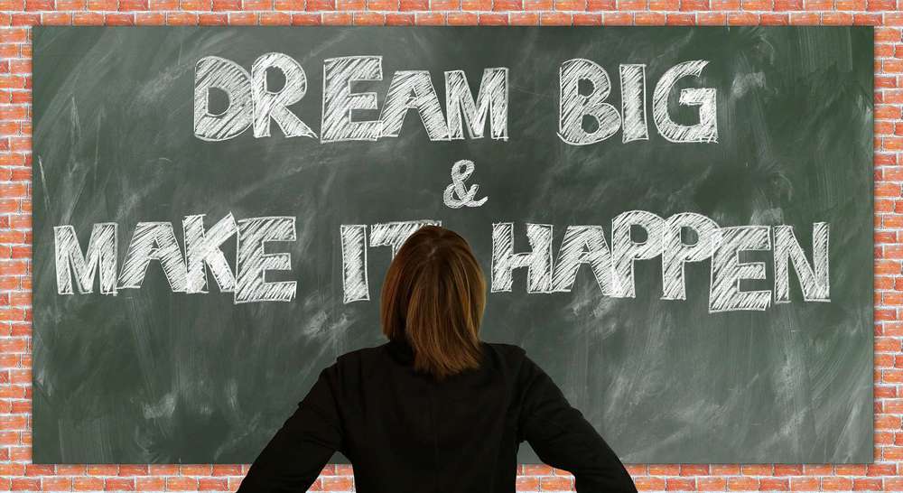 Eine Frau schaut auf eine Tafel, auf der dream big und make it happen geschrieben stehen