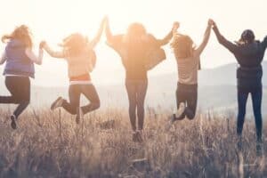 Fünf junge Menschen halten sich an den Händen und springen auf einem Feld