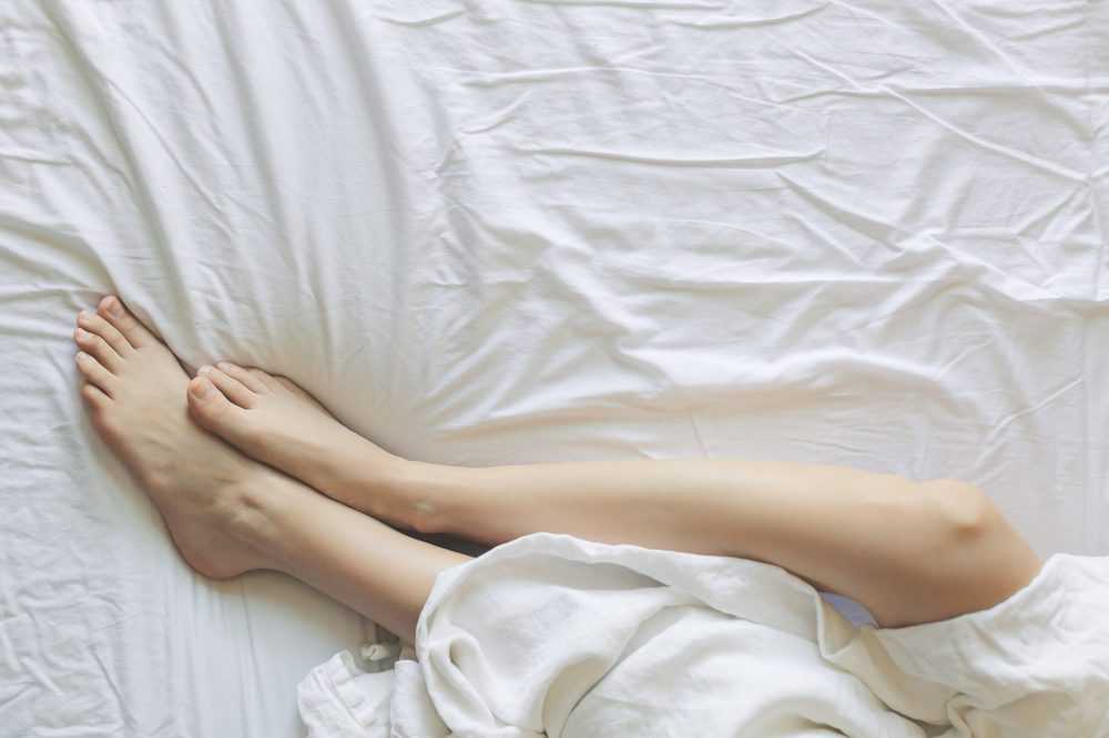 Beine, die unter einer Bettdecke hervorschauen