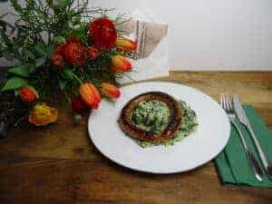 Spinat-Risotto auf weissem Teller mit Bratwurst mit Blumen und Karte auf Holzuntergrund