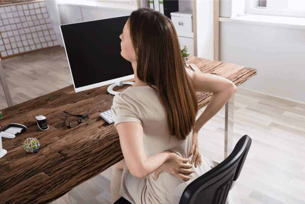 Frau mit Rückenschmerzen vor Computer an Holzschreibtisch