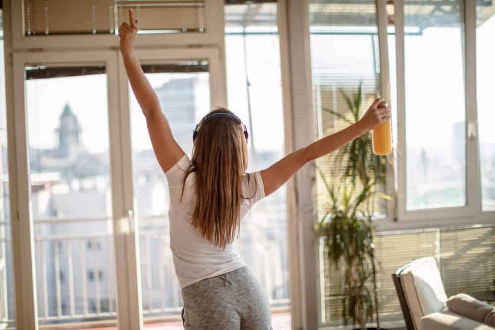 Junge Frau mit Kopfhörern tanzt in ihrer Wohnung