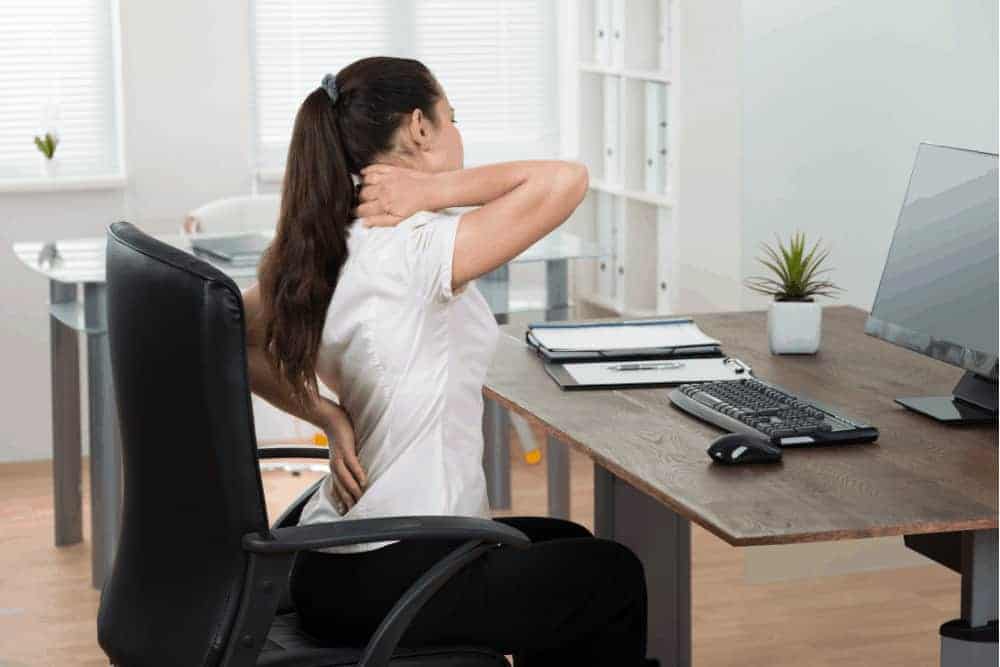 Frau am Arbeitsplatz mit Rückenschmerzen