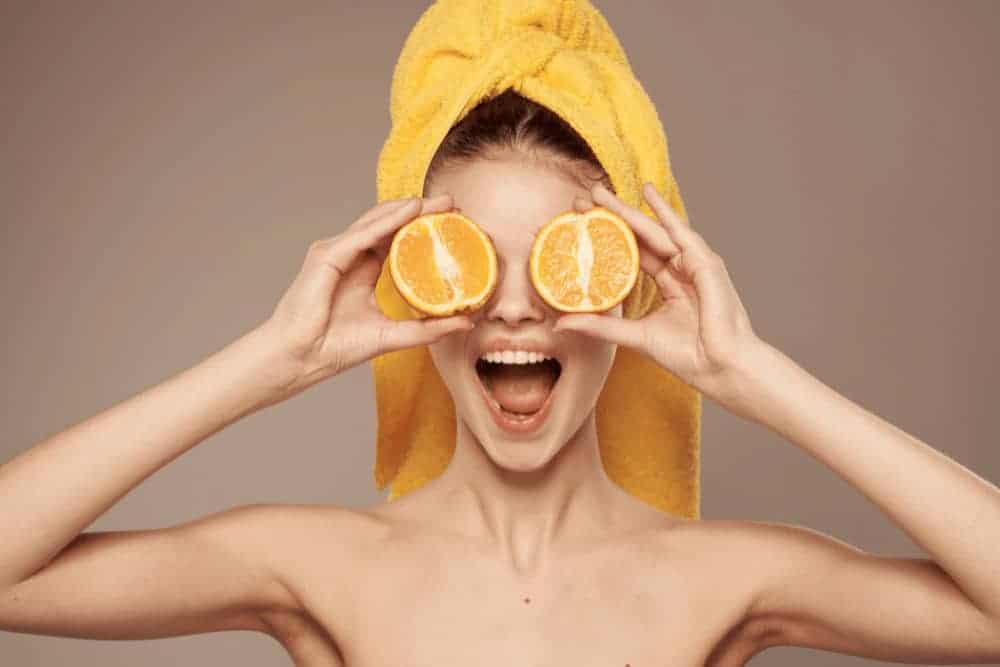 Tipps für schöne Haut junge Frau mit gelbem Handtuch im Haar und zwei Orangenscheiben vor den Augen
