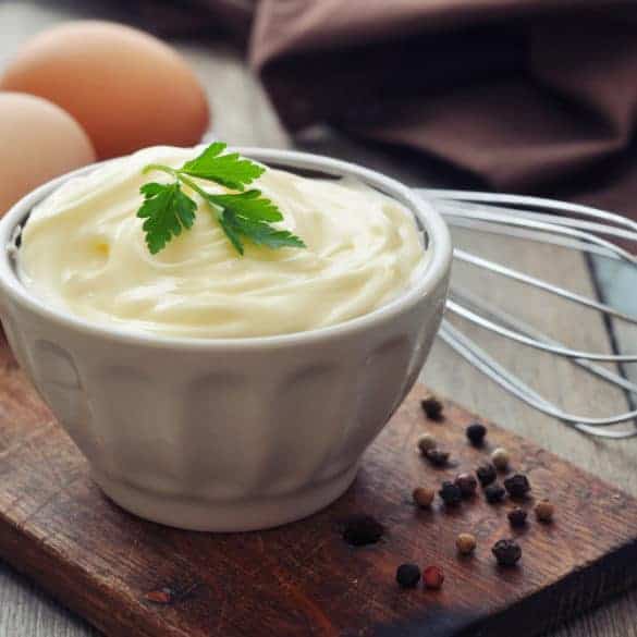 Mayonnaise in weisser Schale mit zwei Eiern und Schwingbesen
