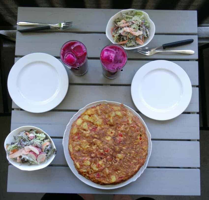 gedeckter Tisch mit Tortilla, zwei Salatschälchen, lila Getränken und zwei weissen Porzellantellern