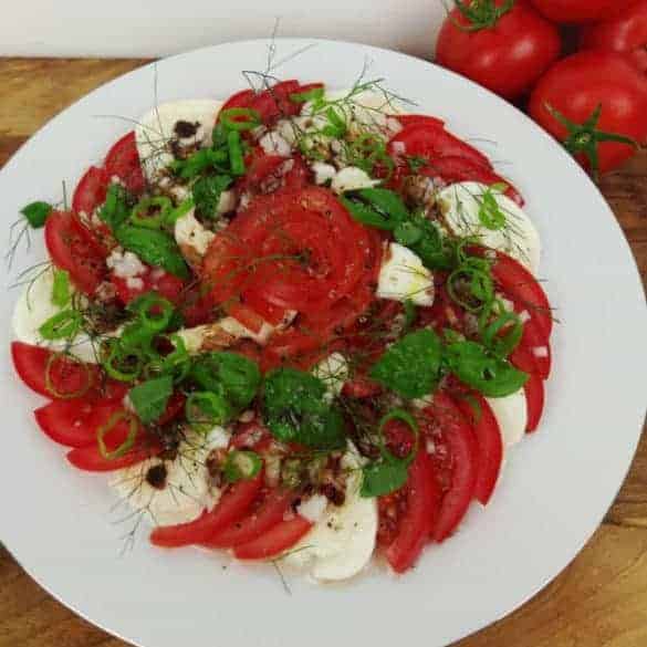 Tomate mit Mozzarella und Kräutern auf weissem Teller mit Silberrand auf Holz