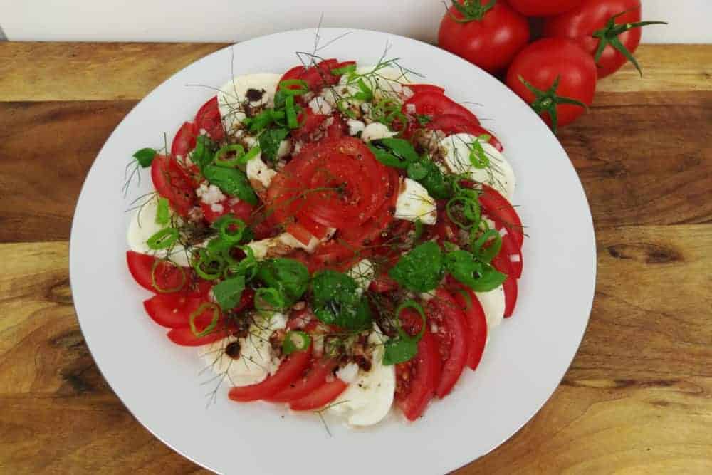 Tomate mit Mozzarella und Kräutern auf weissem Teller mit Silberrand auf Holz
