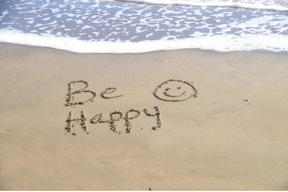 Unkonventionelle Tipps zum Glücklichsein - Be Happy steht im Sand