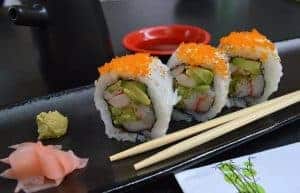 Drei Sushi-Stückchen neben Wasabi und eingelgtem Ingwer auf schwarzer Platte
