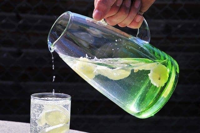 Wasser mit Zitrone in Karaffe wird in Glas ausgegossen