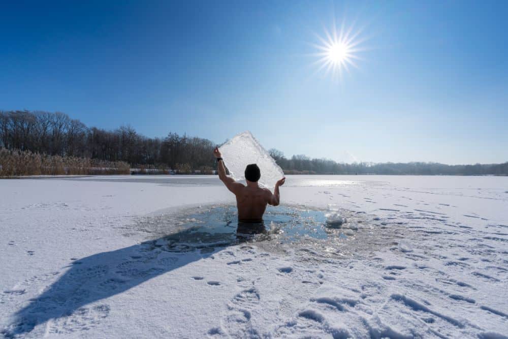 Mann steht in einem vereisten See und hält eine Eisscholle hoch