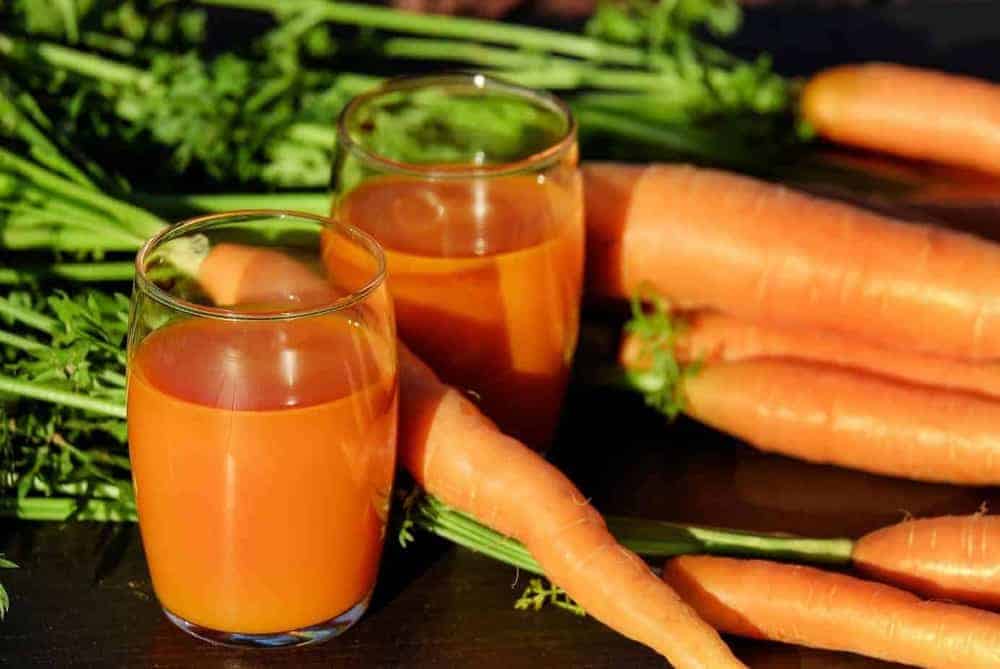 Zwei Gläser mit frischem Karottensaft neben frischen Karotten