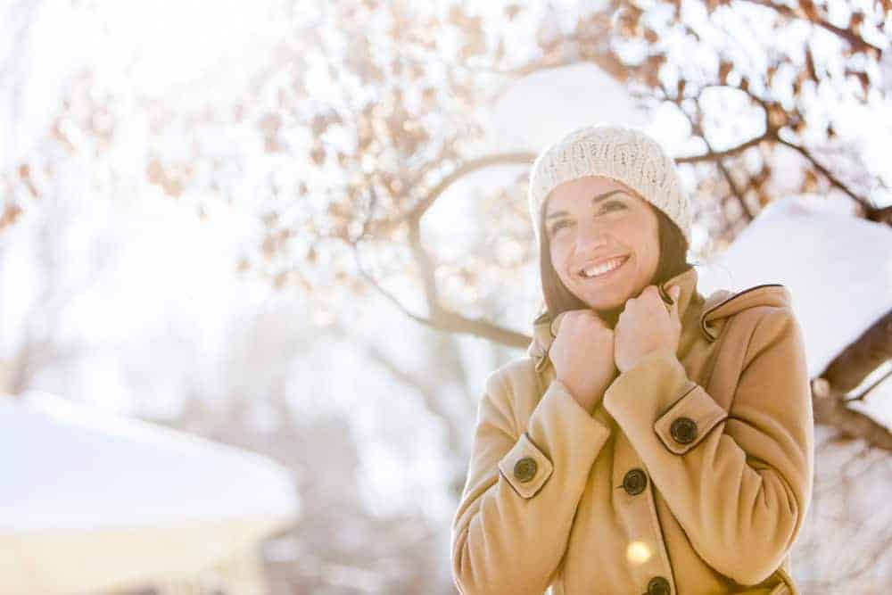 Frau in einem Wintermantel steht vor einem fast vollständig entlaubten Baum