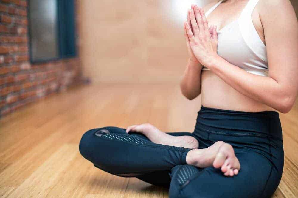 Junge Frau sitzt in Yoga-Haltung auf Parkettboden und faltet die Hände vor ihrer Brust.